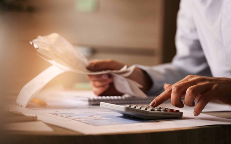 Close-up of economist using calculator while going through bills and taxes in the office.